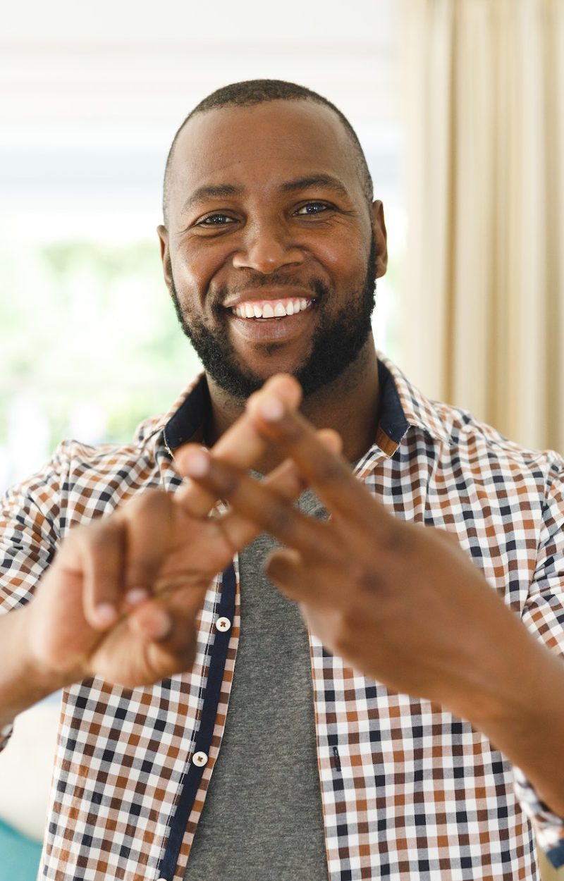 Portrait of african american man smiling and looking at camera in living room talking sign language